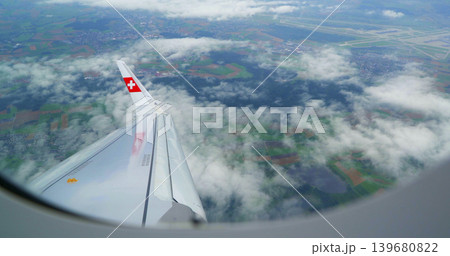 Plane wing viewed from window during flight over fields and clouds near airport in Switzerland 139680822