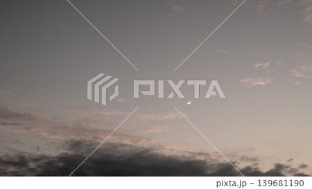 A tranquil dawn sky with a crescent moon and a faint star. The sky transitions from a soft gray to a warm pink near the horizon, with dark, textured clouds below. The scene feels peaceful and ethereal A tranquil dawn sky with a crescent moon and a faint star. The sky transitions from a soft gray to a warm pink near the horizon, with dark, textured clouds below. The scene feels peaceful and ethereal 139681190