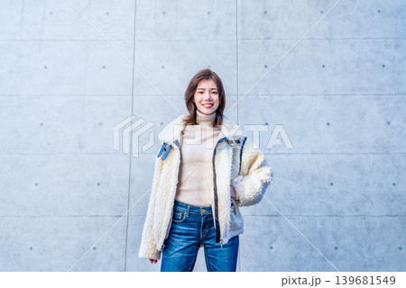 コンクリート壁の前で立つ笑顔の若い女性 コンクリート壁の前で立つ笑顔の若い女性 139681549