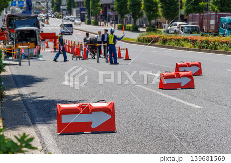 道路工事現場の交通規制と矢印方向板、歩行者を誘導する人 道路工事現場の交通規制と矢印方向板、歩行者を誘導する人 139681569