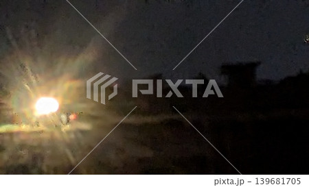 Bright blurry tractor headlight glows in muddy rice field at night. Creative long exposure photography captures rainbow color lens flare reflection over dark rural landscape horizon backdrop. Bright blurry tractor headlight glows in muddy rice field at night. Creative long exposure photography captures rainbow color lens flare reflection over dark rural landscape horizon backdrop. 139681705