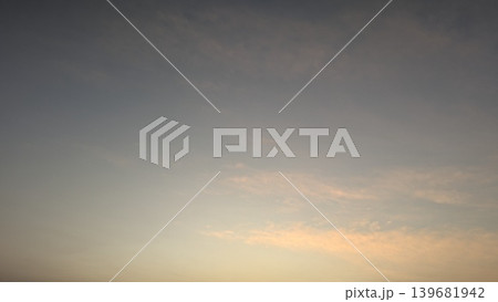 A subtle gradient sky transitions from slate blue to soft peach and gold, featuring delicate wispy clouds near the horizon at sunrise. Beautiful pastel hues of dawn. 139681942