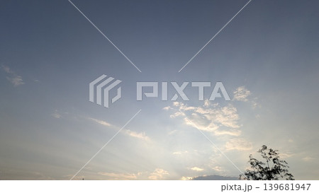 A calm evening sky featuring a subtle gradient from deep blue to soft white and gold at the horizon. Scattered white clouds catch the light, and crepuscular rays fan out from below the frame. A calm evening sky featuring a subtle gradient from deep blue to soft white and gold at the horizon. Scattered white clouds catch the light, and crepuscular rays fan out from below the frame. 139681947