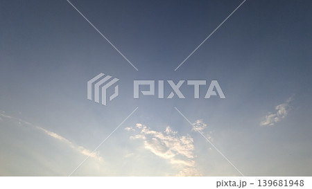 A clear blue sky deepens toward the top, grading down to a bright haze near the bottom horizon. A few scattered, illuminated white cumulus clouds drift in the lower center of the frame. A clear blue sky deepens toward the top, grading down to a bright haze near the bottom horizon. A few scattered, illuminated white cumulus clouds drift in the lower center of the frame. 139681948
