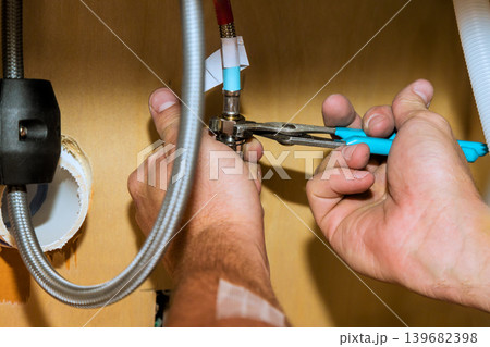 Worker repairs plumbing under sink using tools in kitchen setting 139682398