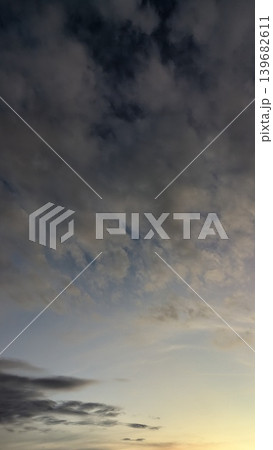 A tranquil sky with light, fluffy clouds. The colors shift from a cool, dusky gray to a hint of pink and yellow at the bottom. A few small, darker clouds add texture to the scene. 139682611