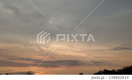 A vast sky is filled with a mix of dark clouds and vibrant, glowing orange and pink hues from a sunset, with a silhouette of trees on the horizon below. The scene is dramatic yet peaceful. 139682614