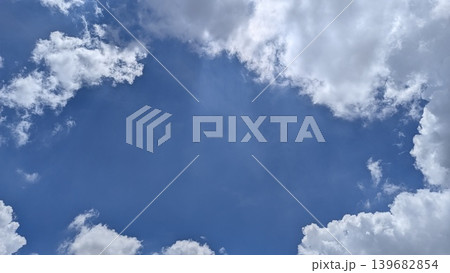 Fluffy white clouds frame a bright, deep blue sky, creating a natural window or copy space in the center. A classic skyscape abstract background for overlay text or design elements. 139682854