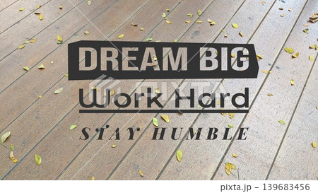 A motivational message DREAM BIG, Work Hard, STAY HUMBLE overlaid on a wooden floor with scattered leaves, inspiring ambition, effort, and modesty. A motivational message DREAM BIG, Work Hard, STAY HUMBLE overlaid on a wooden floor with scattered leaves, inspiring ambition, effort, and modesty. 139683456