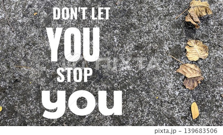 A bold and direct motivational quote, Don't let you stop you, displayed on a textured grey concrete surface with scattered dry leaves. A bold and direct motivational quote, Don't let you stop you, displayed on a textured grey concrete surface with scattered dry leaves. 139683506