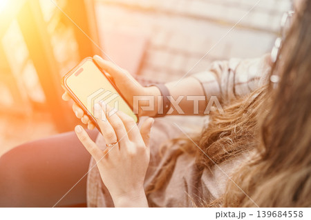 Smartphone mobile technology woman using cellular phone in bright sunny outdoor environment with warm golden lens flare 139684558