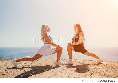 Athletes stretching cliffside Two women perform lunges on a cliff overlooking the ocean during a bright sunny fitness session Athletes stretching cliffside Two women perform lunges on a cliff overlooking the ocean during a bright sunny fitness session 139684583
