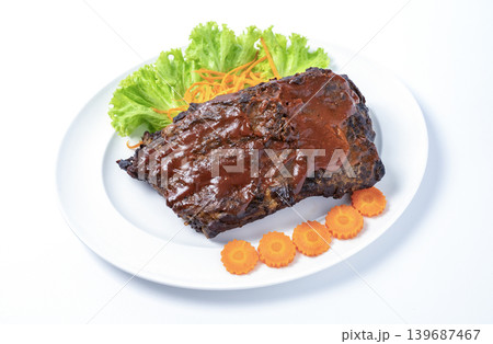 Grilled pork ribs coated in thick BBQ sauce served on a white plate with lettuce and carrot garnish. Professional food photography isolated on white background. Perfect for restaurant menu use. Grilled pork ribs coated in thick BBQ sauce served on a white plate with lettuce and carrot garnish. Professional food photography isolated on white background. Perfect for restaurant menu use. 139687467