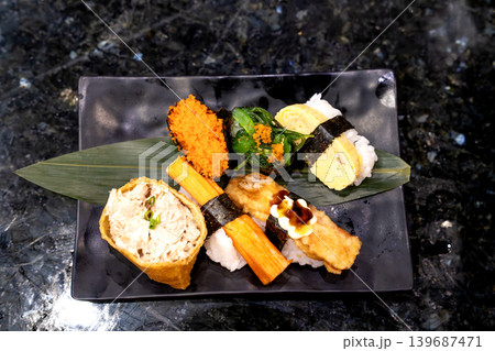 Assorted sushi platter on a black ceramic plate over dark marble background. Includes inari, crab stick nigiri, tamago, fried topping, seaweed salad, and fish roe. Traditional Japanese food garnish. Assorted sushi platter on a black ceramic plate over dark marble background. Includes inari, crab stick nigiri, tamago, fried topping, seaweed salad, and fish roe. Traditional Japanese food garnish. 139687471