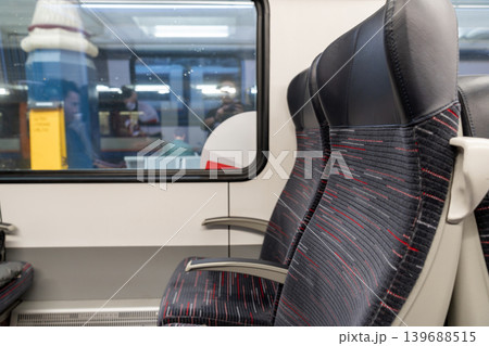 Empty train seats viewed through a window at Liverpool Street Station. Armrests and patterned upholstery visible. Empty train seats viewed through a window at Liverpool Street Station. Armrests and patterned upholstery visible. 139688515