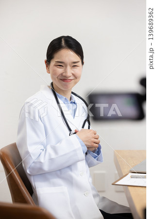 ビデオカメラの前で手振りをつけて話す白衣を着た日本人女性医師 139689362