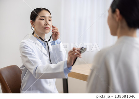 聴診器を使って女性患者を診察する白衣を着た日本人女性医師 聴診器を使って女性患者を診察する白衣を着た日本人女性医師 139691040