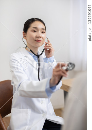 聴診器を使って女性患者を診察する白衣を着た日本人女性医師 聴診器を使って女性患者を診察する白衣を着た日本人女性医師 139691042