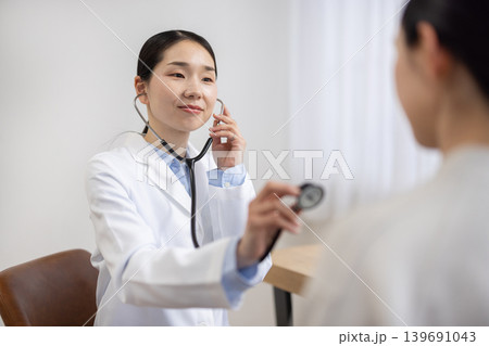聴診器を使って女性患者を診察する白衣を着た日本人女性医師 聴診器を使って女性患者を診察する白衣を着た日本人女性医師 139691043