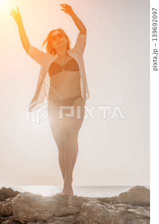 Woman beach sunset dancing on rocks by the sea during golden hour for summer vacation joy Woman beach sunset dancing on rocks by the sea during golden hour for summer vacation joy 139692097