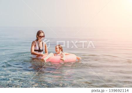Mother daughter ocean playing together with pink inflatable ring in calm sea water during summer vacation for family bonding Mother daughter ocean playing together with pink inflatable ring in calm sea water during summer vacation for family bonding 139692114