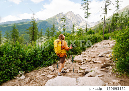 Young woman traveler hiking poles on trail among the mountains. Hiking. Active lifestyle. 139693182