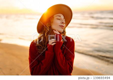 Beautiful curly woman on beach in cold sunny weather, deeply breathing fresh ocean breeze. Lifestyle 139693494