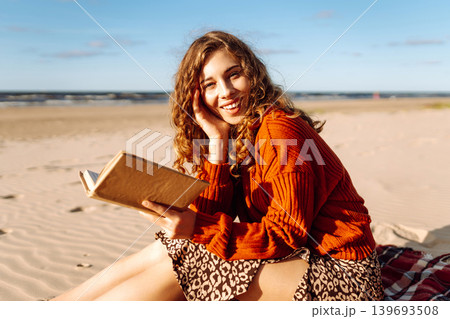 Woman enjoys reading book on sandy beach during with gentle waves in the background, radiating joy. Woman enjoys reading book on sandy beach during with gentle waves in the background, radiating joy. 139693508