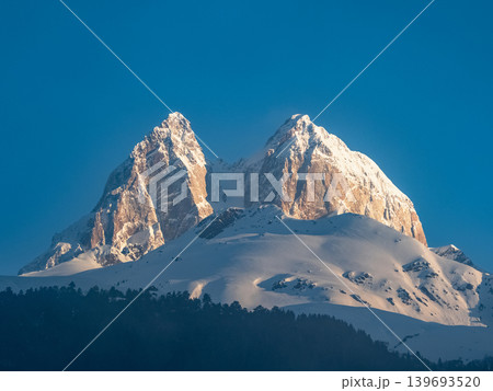 Mount Ushba in Svaneti, Georgia. Snow-capped peaks rise sharply against a clear blue sky Mount Ushba in Svaneti, Georgia. Snow-capped peaks rise sharply against a clear blue sky 139693520