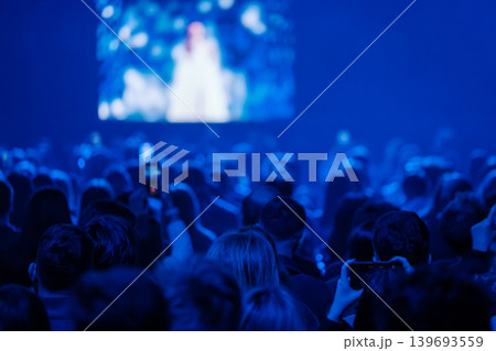Blue concert audience watching stage performance, crowd recording with phones in dark venue 139693559