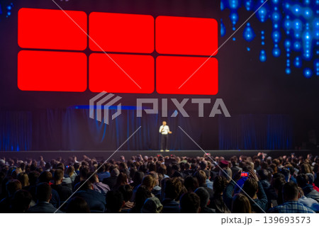 Keynote speaker on stage presenting to large audience at conference with vibrant LED screens 139693573