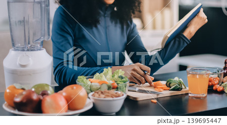 Young nutritionist showing bell peppers during an online video call consulting about healthy eating, sitting at home at a table with vegetables, laptop and measuring tape 139695447