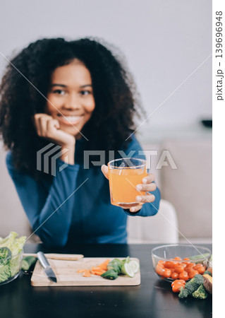 Young nutritionist showing bell peppers during an online video call consulting about healthy eating, sitting at home at a table with vegetables, laptop and measuring tape Young nutritionist showing bell peppers during an online video call consulting about healthy eating, sitting at home at a table with vegetables, laptop and measuring tape 139696948