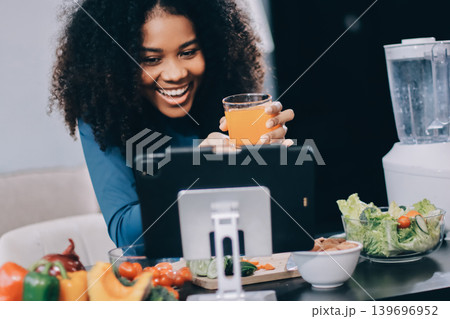 Young nutritionist showing bell peppers during an online video call consulting about healthy eating, sitting at home at a table with vegetables, laptop and measuring tape Young nutritionist showing bell peppers during an online video call consulting about healthy eating, sitting at home at a table with vegetables, laptop and measuring tape 139696952
