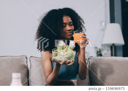 Young nutritionist showing bell peppers during an online video call consulting about healthy eating, sitting at home at a table with vegetables, laptop and measuring tape 139696973