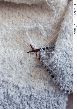 White and grey boucle knitting with knitting needles. Soft white knitwear with wooden needles. Knitting pattern background. Knitting lifestyle. Cozy hobby. Warm knitwear. Craft product concept 139697401