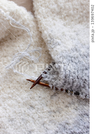 White and grey boucle knitting with knitting needles. Soft white knitwear with wooden needles. Knitting pattern background. Knitting lifestyle. Cozy hobby. Warm knitwear. Craft product concept White and grey boucle knitting with knitting needles. Soft white knitwear with wooden needles. Knitting pattern background. Knitting lifestyle. Cozy hobby. Warm knitwear. Craft product concept 139697402
