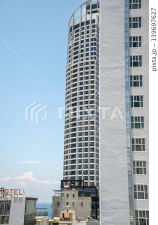 Tall modern residential and hotel skyscraper surrounded by dense urban architecture in Nha Trang Vietnam with tropical coastal atmosphere and clear blue sky. Tall modern residential and hotel skyscraper surrounded by dense urban architecture in Nha Trang Vietnam with tropical coastal atmosphere and clear blue sky. 139697627