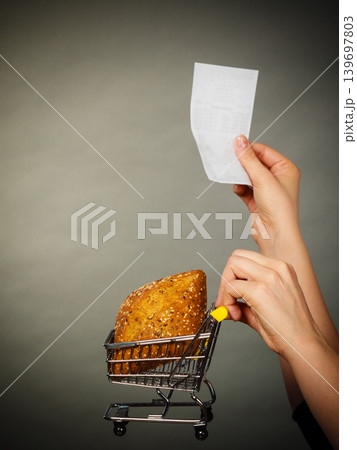 Hand holding shopping cart with bread and bill Hand holding shopping cart with bread and bill 139697803