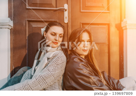 Women sunset friends sitting back to back against rustic wooden door in warm autumn light during golden hour Women sunset friends sitting back to back against rustic wooden door in warm autumn light during golden hour 139697809