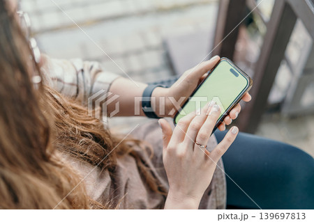 Smartphone mockup woman uses mobile device with green screen for content placement while sitting in outdoor environment Smartphone mockup woman uses mobile device with green screen for content placement while sitting in outdoor environment 139697813