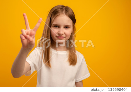 Adorable Girl Flashes A Victory Sign With Fingers Against A Vibrant Orange Background Adorable Girl Flashes A Victory Sign With Fingers Against A Vibrant Orange Background 139698404