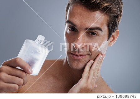 Studio, portrait and man with aftershave for beauty, grooming and facial treatment or cologne. Model, face and happy with bottle for cosmetics product, fragrance and male skincare by gray background Studio, portrait and man with aftershave for beauty, grooming and facial treatment or cologne. Model, face and happy with bottle for cosmetics product, fragrance and male skincare by gray background 139698745