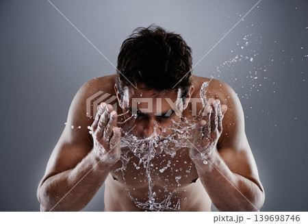Water drops, splash and man cleaning face for bathroom routine, dermatology cleanse or beauty treatment for skincare. Studio, moisture and model facial wash, hygiene and grooming on grey background Water drops, splash and man cleaning face for bathroom routine, dermatology cleanse or beauty treatment for skincare. Studio, moisture and model facial wash, hygiene and grooming on grey background 139698746