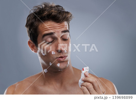 Man, face and shave cuts or paper for hair removal hygiene or injury with blood, tissue or maintenance. Male person, grey background and dermatology with beard or clean health, studio or mockup space 139698899