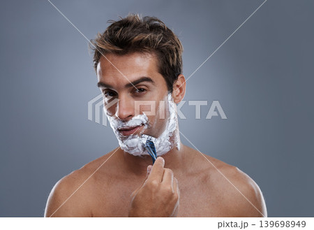 Man, razor and face with shaving in studio portrait for grooming, skin and wellness by grey background. Person, model and blade with cream, facial hair removal and foam product for hygiene with beard Man, razor and face with shaving in studio portrait for grooming, skin and wellness by grey background. Person, model and blade with cream, facial hair removal and foam product for hygiene with beard 139698949
