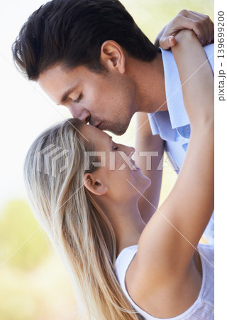 Happy couple, kiss and hug in nature for romance, support or affection in outdoor bonding. Young man and woman forehead with smile for embrace, comfort or love in forest or woods together on date 139699200