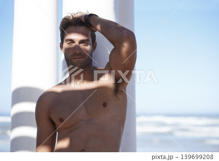 Smile, shirtless and portrait of man outdoor by pillars at beach with confidence on vacation. Happy, model and handsome young male person by wall at ocean or sea for holiday or weekend trip. Smile, shirtless and portrait of man outdoor by pillars at beach with confidence on vacation. Happy, model and handsome young male person by wall at ocean or sea for holiday or weekend trip. 139699208