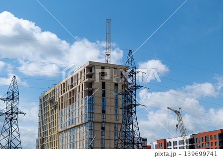 Construction is underway for a new house with cranes and power lines visible under a bright blue sky and clouds Construction is underway for a new house with cranes and power lines visible under a bright blue sky and clouds 139699741