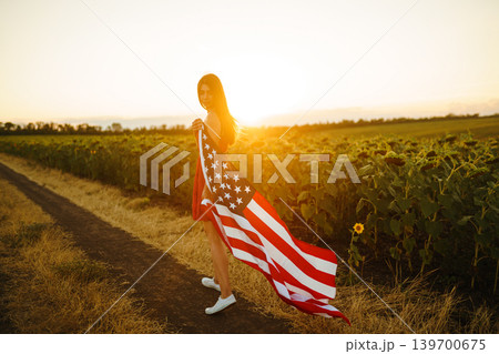 Beautiful girl in hat with the American flag in a sunflower field. 4th of July. Fourth of July. Independence Day. 139700675
